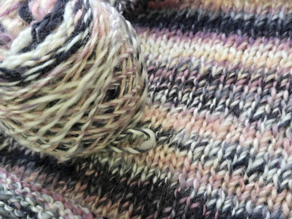 The yarn and the beginning of a knit panel in black, white, and pink